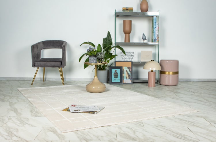 Heller Wohnbereich mit geometrisch gemustertem Teppich, samtbezogenem Stuhl, Metallregal, Beistelltisch und verschiedenen Dekorationsgegenständen.
