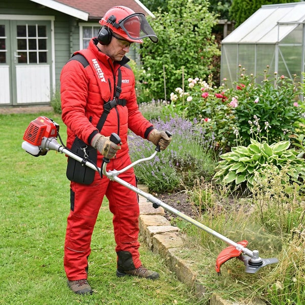Mann mit Schutzhelm und Trimmer beim Rasentrimmen im Garten