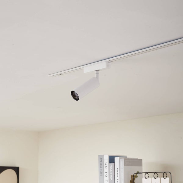 Heller und organisierter Raum mit einem modernen zylindrischen Schienenspot aus Metall an einer weißen Deckenschiene über einem Bücherregal.
