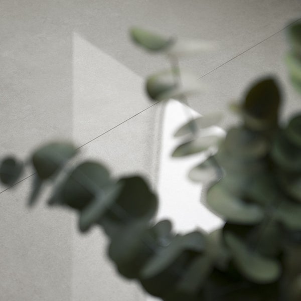 Nahaufnahme einer glatten Betonoptik Fliese mit sichtbarer Fuge und unscharfen Pflanzen im Vordergrund