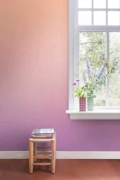 Raum mit rosa Farbverlauf an der Wand, Fenster, Blumen und einem kleinen Hocker mit Büchern.