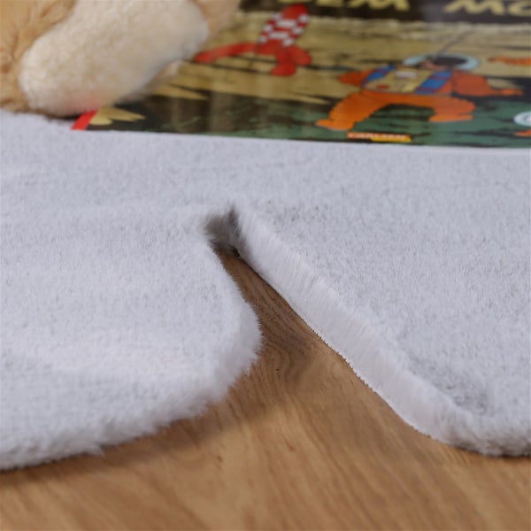 Ein flauschiger Teppich in Lammfelloptik auf einem Holzboden mit einem Kinderbuch im Hintergrund.