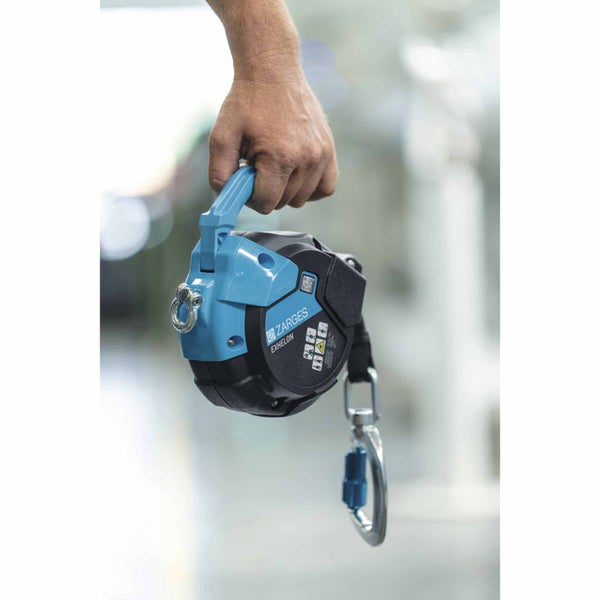 Zarges Höhensicherungsgerät Exhelon in der Hand gehalten mit Karabinerhaken und Sicherheitshinweisen.