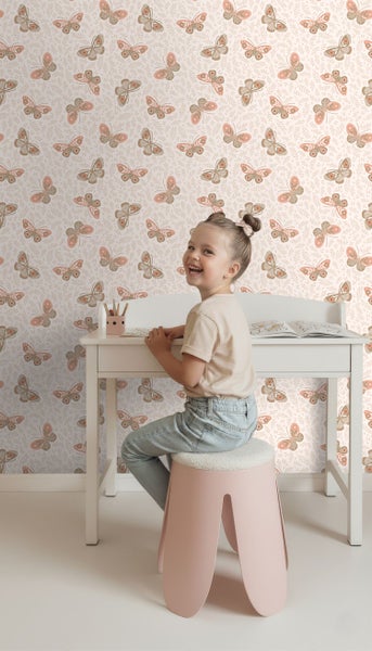 Mädchen sitzt an einem Schreibtisch vor einer Tapete mit Schmetterlingsmuster.