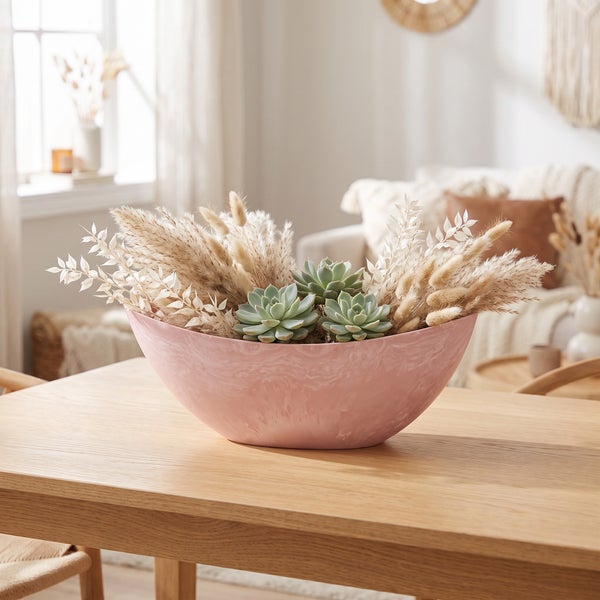Dekorative Schale mit Sukkulenten und Trockenblumen auf einem Holztisch in einem hellen Wohnzimmer.