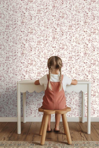 Kinderzimmer mit einer Vliestapete mit floralem Muster und Hasen, weißem Schreibtisch und einem hölzernen Hocker.