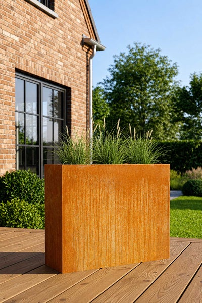 Rechteckiger Pflanzkübel in Edelrost-Optik auf einer Holzterrasse im Garten, bepflanzt mit Ziergräsern.