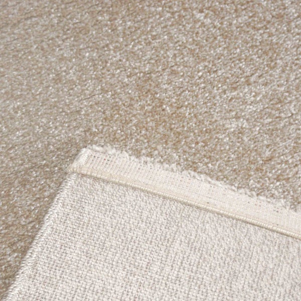 Nahaufnahme eines beigen Plüschteppichs mit weicher Oberflächenstruktur und gewebter Rückseite.