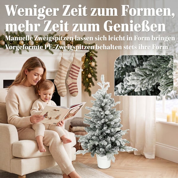 Mutter und Kind sitzen vor dem Kamin und lesen ein Buch neben einem künstlichen, verschneiten Weihnachtsbaum im Topf.