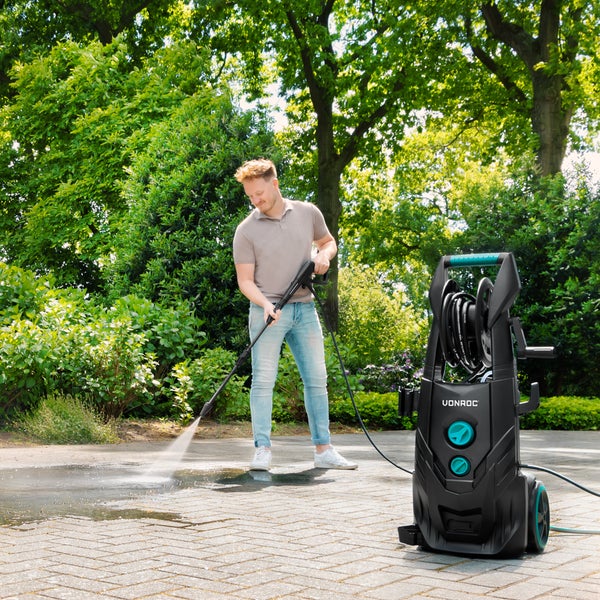 Ein Mann reinigt eine Steinterrasse mit einem Vonroc Hochdruckreiniger in einem hellen, grünen Garten.