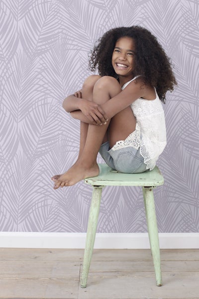 Ein Mädchen sitzt auf einem Hocker vor einer mit Blättern bedruckten Tapete.