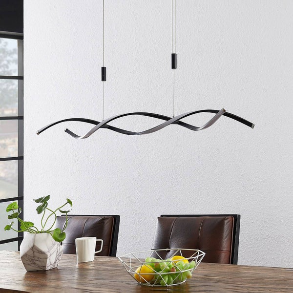 Moderne LED-Pendelleuchte in Wellenform über einem Esstisch aus Holz mit braunen Lederstühlen und einer Obstschale.