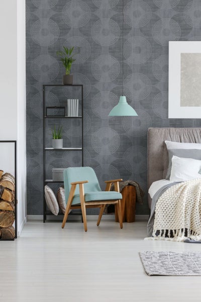 Schlafzimmer mit Bett, Sessel, Regal und gemusterter Tapete