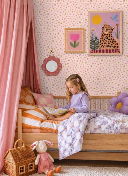 Kindertapete mit Sternenmuster in einem hell gestalteten Kinderzimmer mit einem Mädchen im Holzbett und textilen Dekorationselementen.