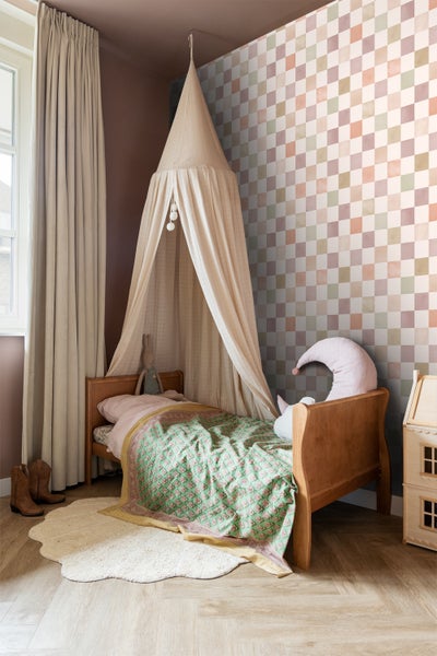 Einladendes Kinderzimmer mit Himmelbett, gemusterter Tapete und Holzmöbeln für eine warme Atmosphäre.