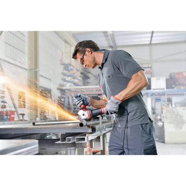 Handwerker trennt ein Metallrohr mit einem Winkelschleifer in einer Werkstatt, starker Funkenflug.