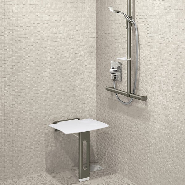 Barrierefreie Dusche mit klappbarem Duschsitz, Bodenstütze, Duschstange, Haltegriff und Handbrause vor hellen Mosaikfliesen.