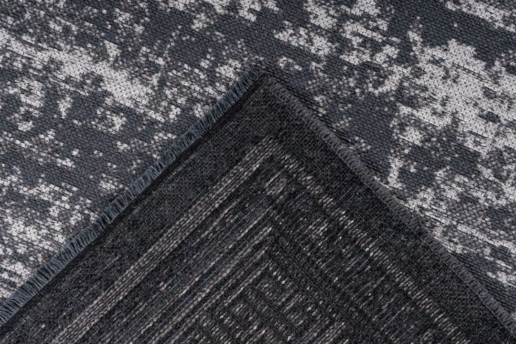 Nahaufnahme eines gewebten Teppichs mit abstraktem Vintage-Muster, wobei eine umgeschlagene Ecke die strukturierte Rückseite zeigt.