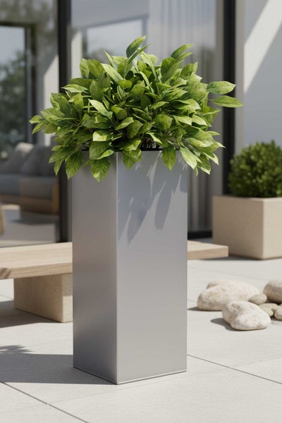 Hoher rechteckiger Pflanzkübel aus Metall mit grüner Pflanze auf einer modernen hellen Terrasse mit Steinboden und Holzbank.