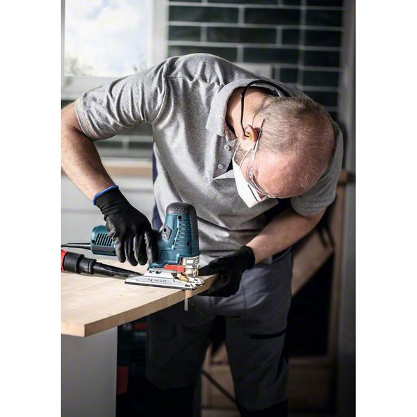 Mann arbeitet mit Stichsäge an einem Holzbrett, Schutzbrille und Handschuhe werden getragen