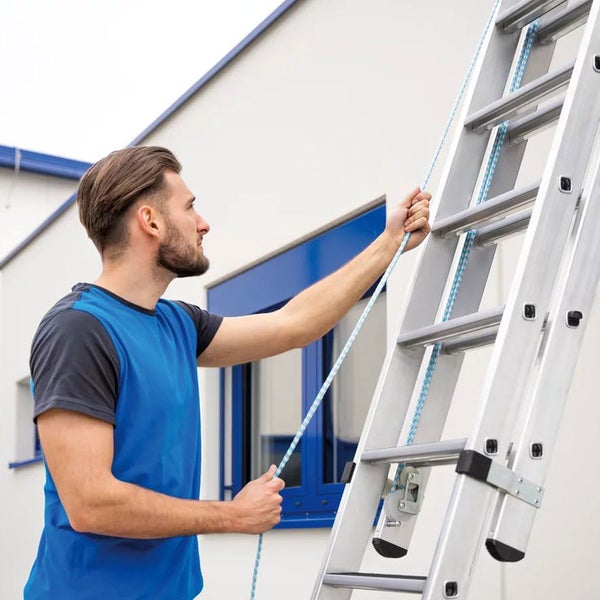 Mann bedient eine Aluminiumleiter mit Seilzug vor einem Gebäude.
