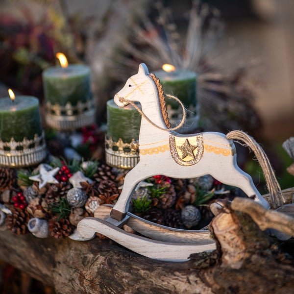 Weihnachtliche Dekoration mit Kerzen, Tannenzapfen und Holzschaukelpferd.
