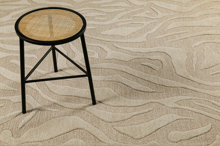 Moderner Teppich mit Wellenmuster in Hoch-Tief-Optik und runder Hocker mit Sitzfläche aus Wiener Geflecht und schwarzem Metallgestell.