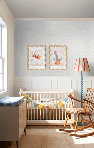 Helles Kinderzimmer mit Gitterbett aus Holz, gepunkteter Tapete, Schaukelstuhl aus Holz und einer Stehlampe mit gestreiftem Schirm.