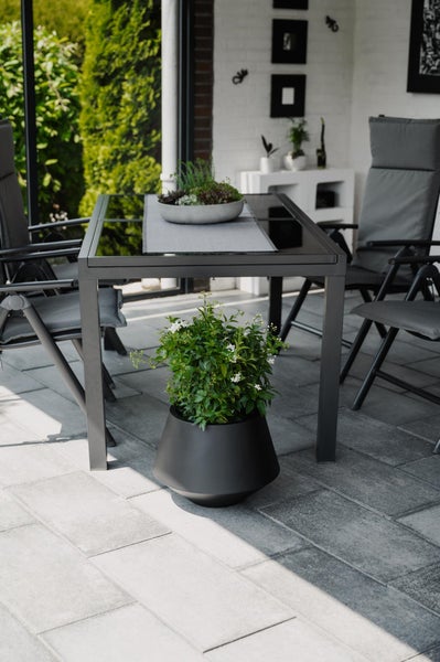 Dunkler Metalltisch mit Gartenstühlen und einem großen dunklen Blumentopf auf einer Steinterrasse im Freien.