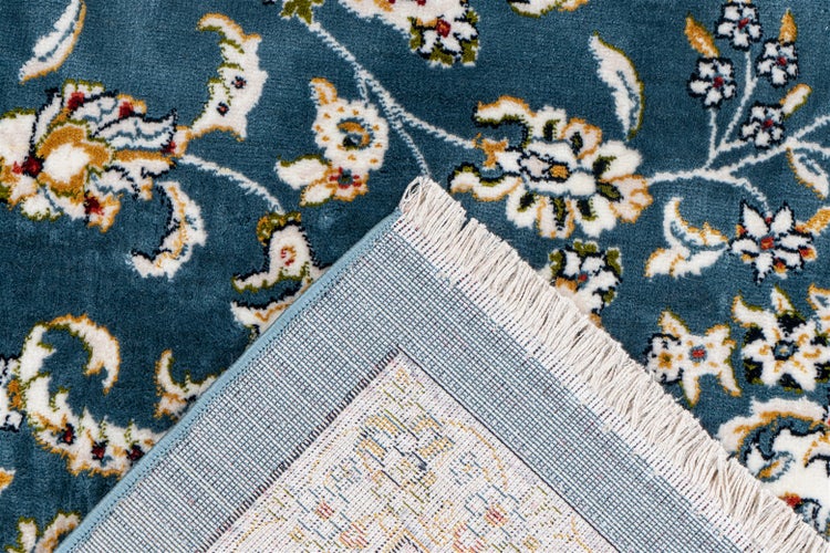 Detailansicht eines blauen Teppichs mit floralem Muster, Fransen und Teppichrücken.