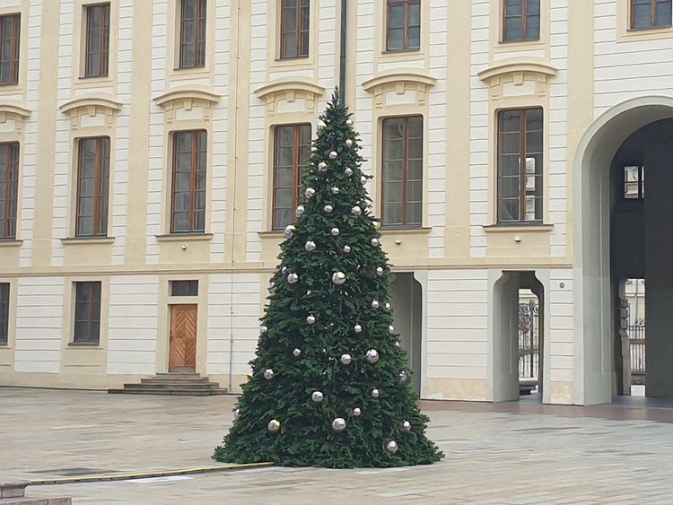 Großer geschmückter Weihnachtsbaum mit silbernen Kugeln vor einer historischen Fassade auf einem gepflasterten Platz.