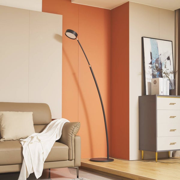 Moderne LED-Bogenleuchte in einem hellen Wohnzimmer mit braunem Ledersofa und grauem Sideboard vor einer beige-orangen Wand.