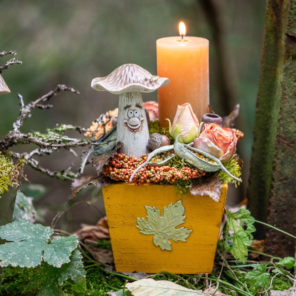 Dekorative Herbstszene mit Pilzfigur, Kerze und Blumenarrangement in einem Topf