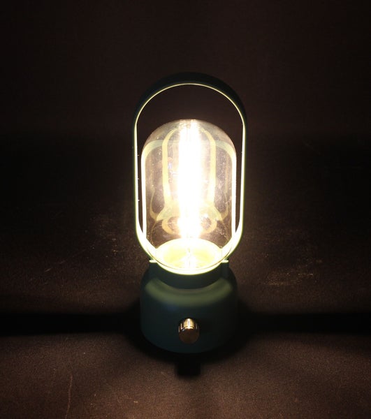 Tragbare LED-Laterne in Dunkelgrün mit Tragebügel und eingeschaltetem LED-Leuchtmittel.