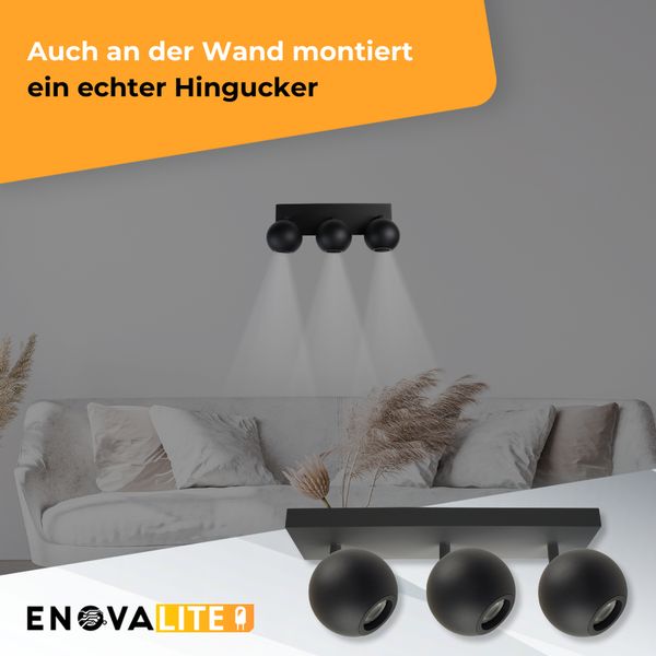 Wohnzimmer mit Sofa und an der Wand montierter, schwarzer EnovaLite Lampe mit drei Leuchten