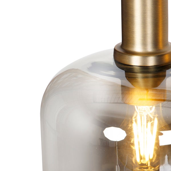 Nahaufnahme einer Glaspendelleuchte mit Messingaufhängung und leuchtendem Leuchtmittel