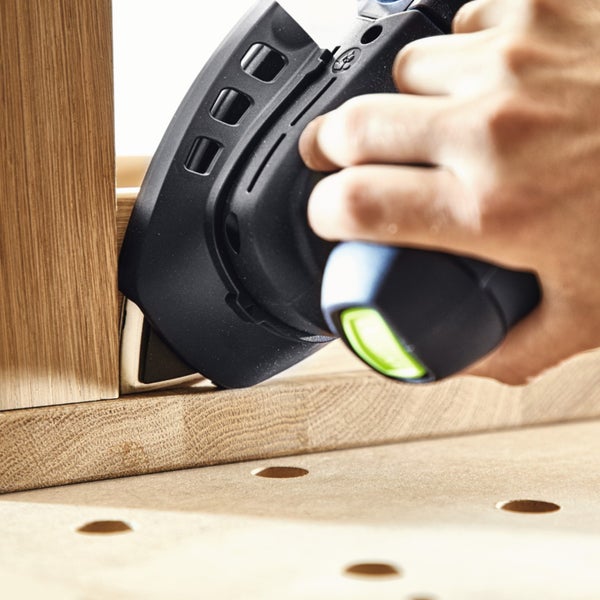 Eine Hand führt einen Multischleifer zum Schleifen einer Innenecke an einem Holzwerkstück auf einer Werkbank.
