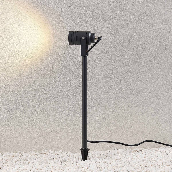 Schwarzer LED-Gartenstrahler mit Erdspieß im Kiesbett, der eine strukturierte Außenwand beleuchtet.