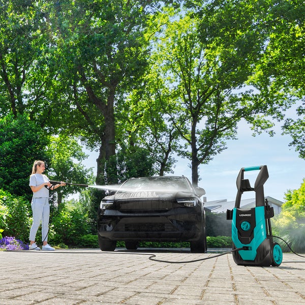 Eine Person wäscht ein Auto auf einer gepflasterten Einfahrt mit einem elektrischen Hochdruckreiniger der Marke Vonroc im Freien.