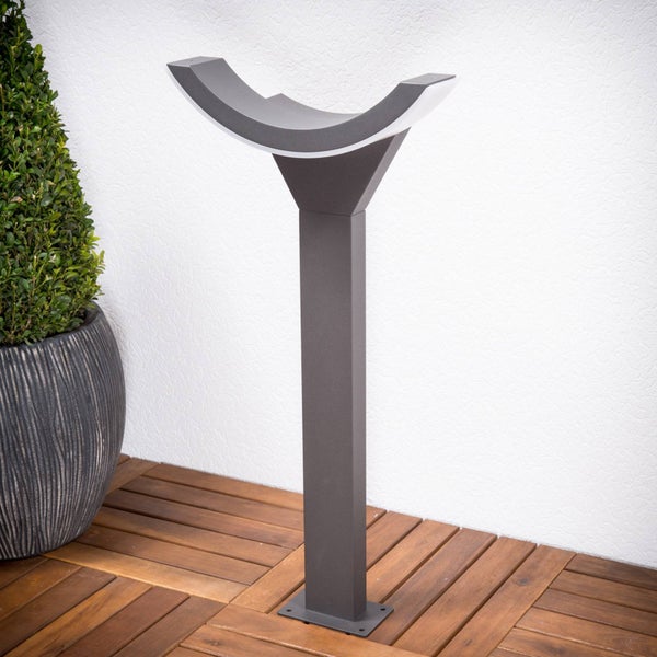 Moderne graue Wegeleuchte in U-Form auf einer Holzterrasse neben einer Pflanze im Topf.