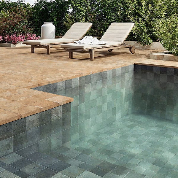 Poolterrasse mit Natursteinplatten und angrenzendem gefliesten Poolbereich mit Liegestühlen im Garten.