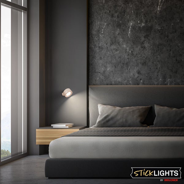 Moderne Schlafzimmer-Beleuchtung mit runder Briloner Sticklights Wandleuchte an dunkelgrauer Wand neben gepolstertem Bett und Holz-Nachttisch.