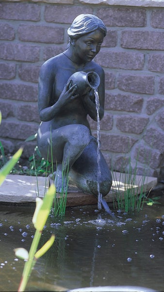 Gartenfigur als Wasserspiel: Kniende Frau mit Krug am Gartenteich, Wasser fließt aus dem Krug in den Teich.
