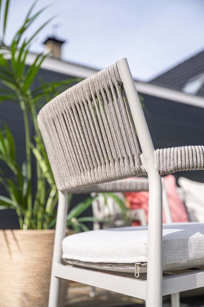 Nahaufnahme eines Gartenstuhls mit Metallgestell, Seilbespannung und Sitzkissen in einem hellen Außenbereich neben einer Pflanze.