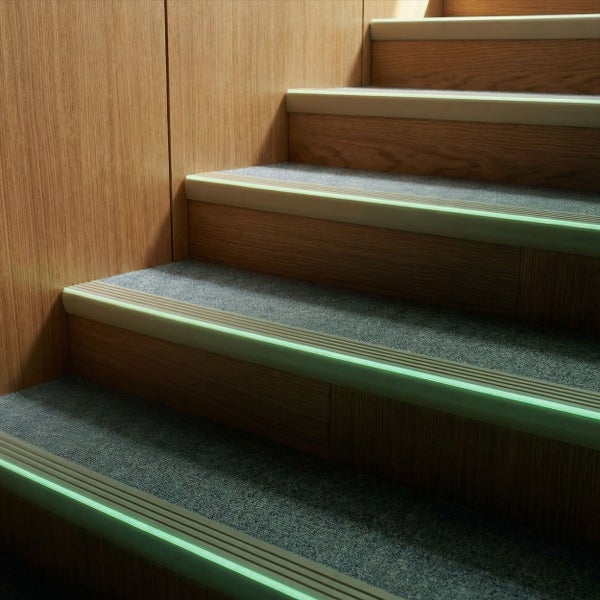 Holztreppe mit Teppichstufenmatten und nachleuchtenden Kantenprofilen für erhöhte Sicherheit und Orientierung im Dunkeln.
