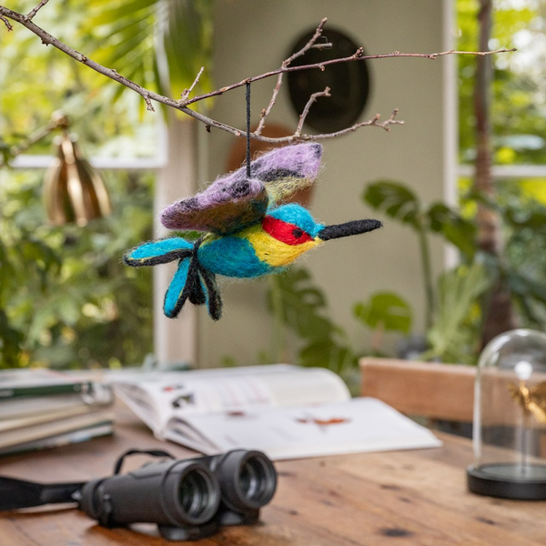 Dekorativer Filz-Kolibri hängt an einem Ast über einem Tisch