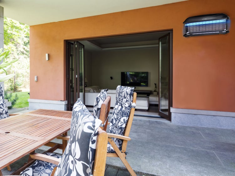 Außenbereich mit Holztisch, Stühlen mit Kissen und elektrischer Insektenfalle an der Wand