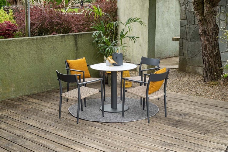Gartenmöbel Set mit rundem Tisch und vier Stühlen mit Armlehnen auf einem runden Teppich auf einer Holzterrasse.
