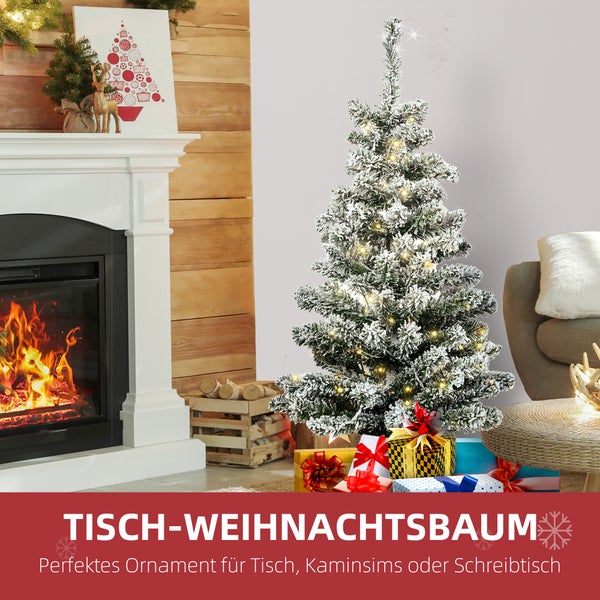 Kleiner künstlicher Weihnachtsbaum mit Schnee und LED-Lichtern neben Geschenken vor einem Kamin.