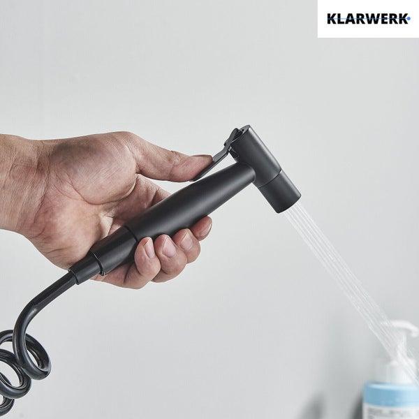 Hand hält eine schwarze Klarwerk Bidet-Handbrause mit Wasserstrahl. Klarwerk Logo.